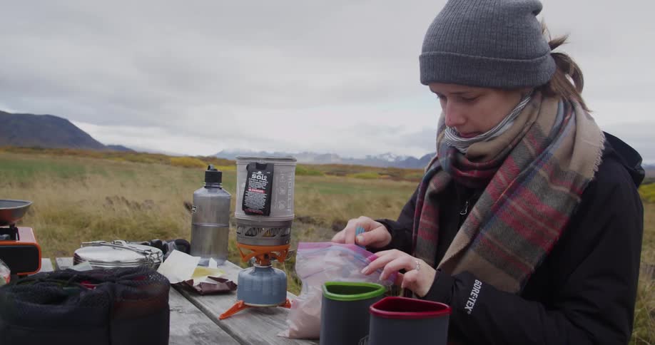A woman spoons something out of a bag into a cup