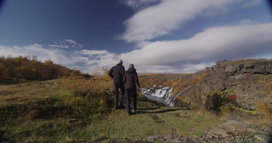 Two people hike over to a small stream of water holding hands