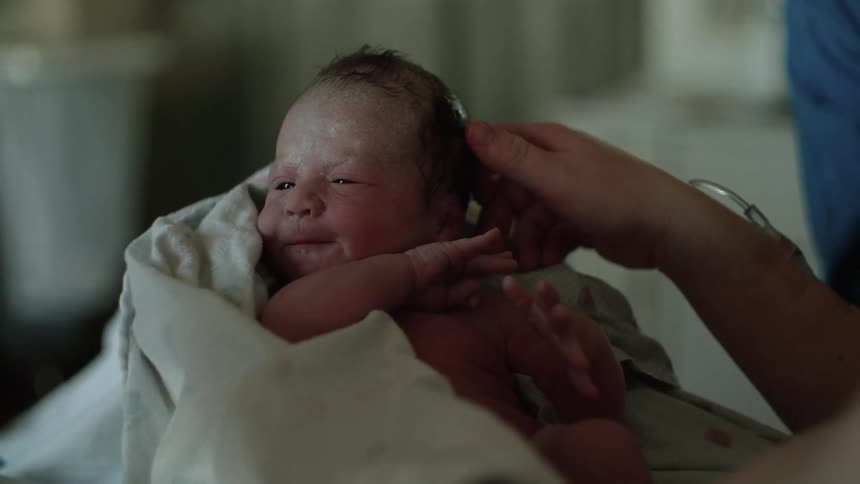 A moms hands hold and caress her newborn baby
