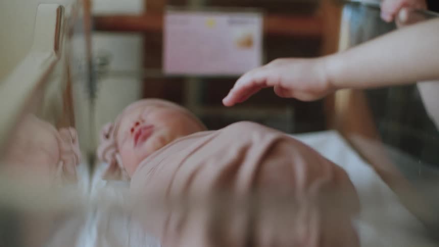 Big sister patting a sleeping newborn inside a crib in the hospital