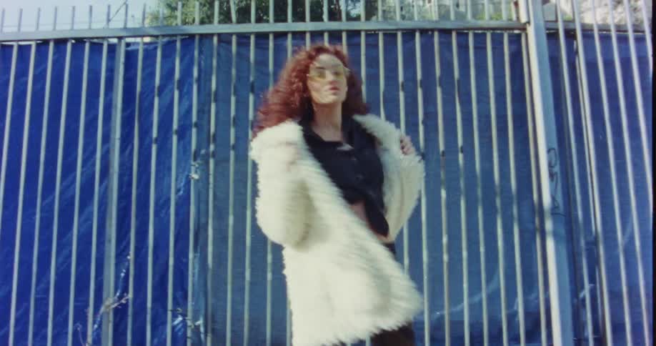 A woman stops walking turns and poses in front of a fence