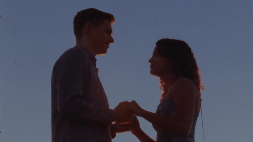 Silhouette of a young couple holding hands against a blue sky at sunset