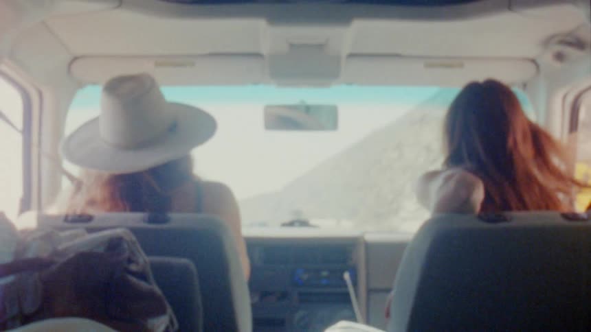 Two women dance in their seats while driving along a highway
