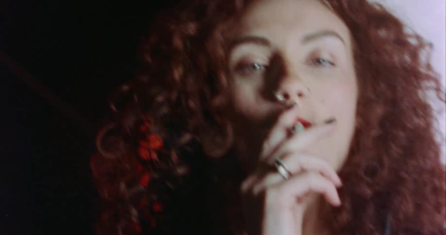 Woman with red curl hair and makeup smokes cigarette and looks at camera