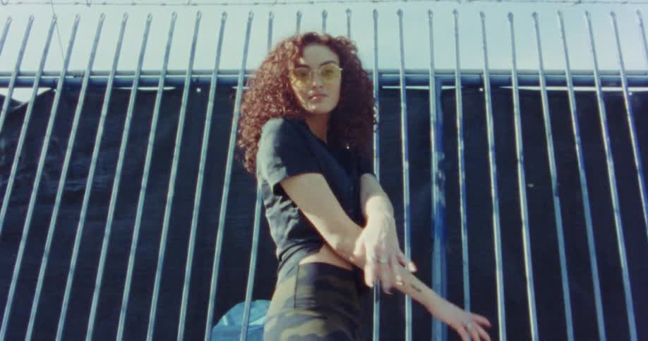 A woman dances in front of a fence with metal bars on a bright sunny day