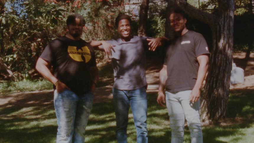 Three men stand beside each other outside posing for a photograph