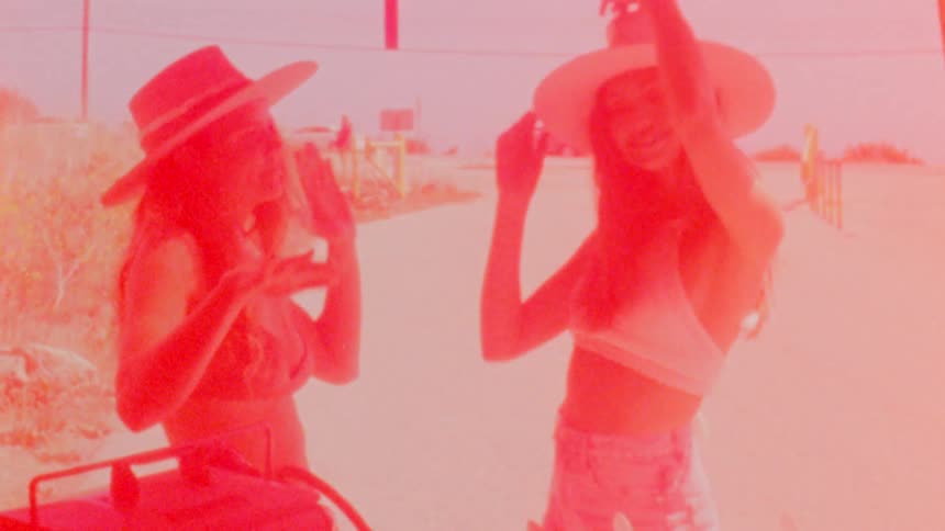Two young friends wearing sun hats dancing near the beach caught on vintage film