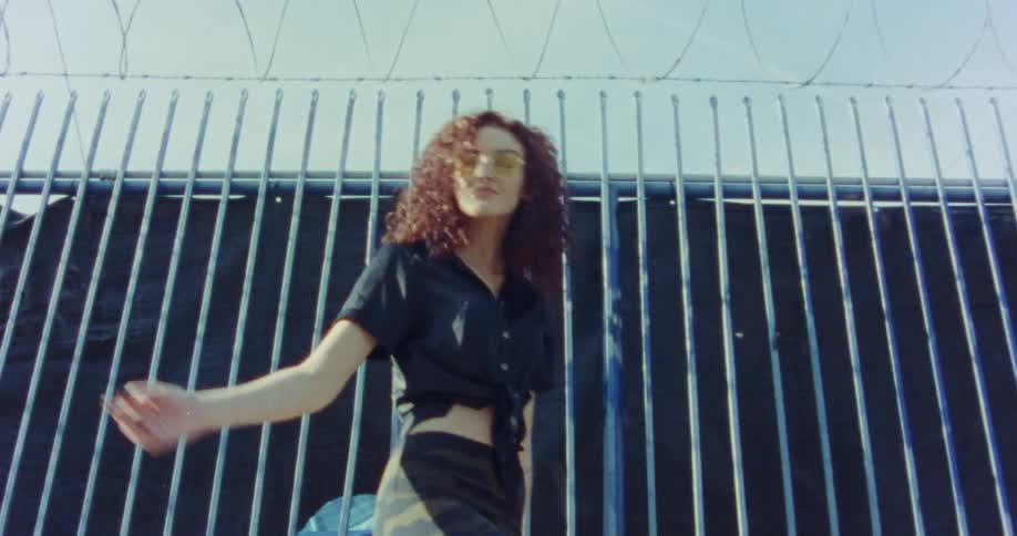 A woman dancing in front of a fence pauses and looks back