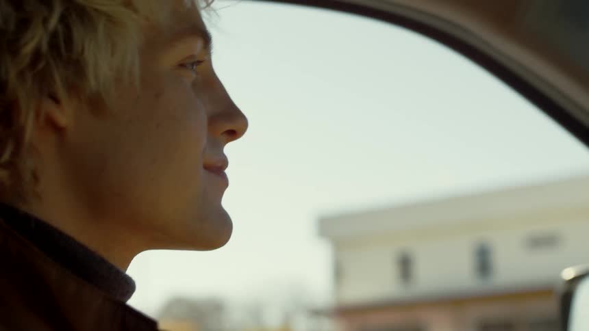 Side view of clean shaven blonde man driving car in the street