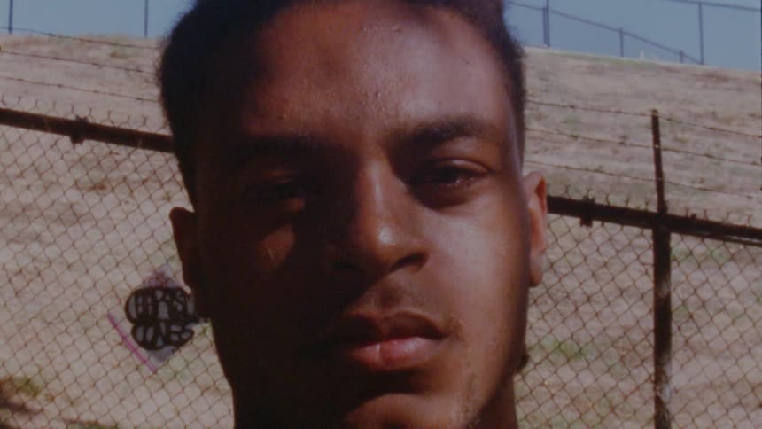A man stands on the side of a hill near a chain link fence with barbed wire