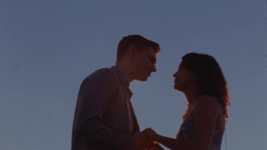A man and a woman are outside holding hands and kissing