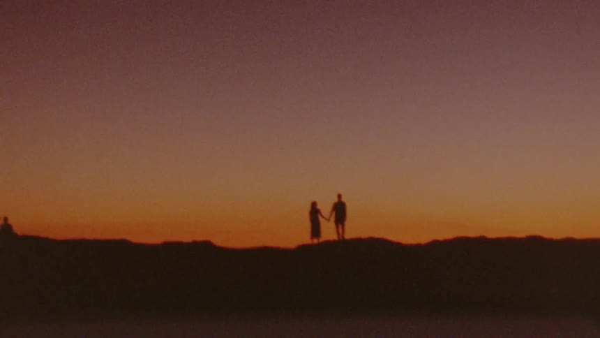 A couple hold hands as they stand on top of a hill at dusk