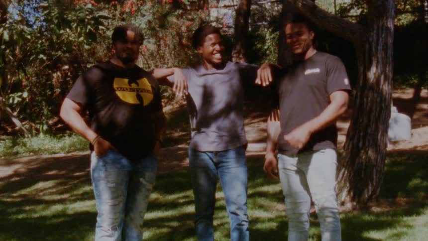 Three men that are friends are standing together outdoors