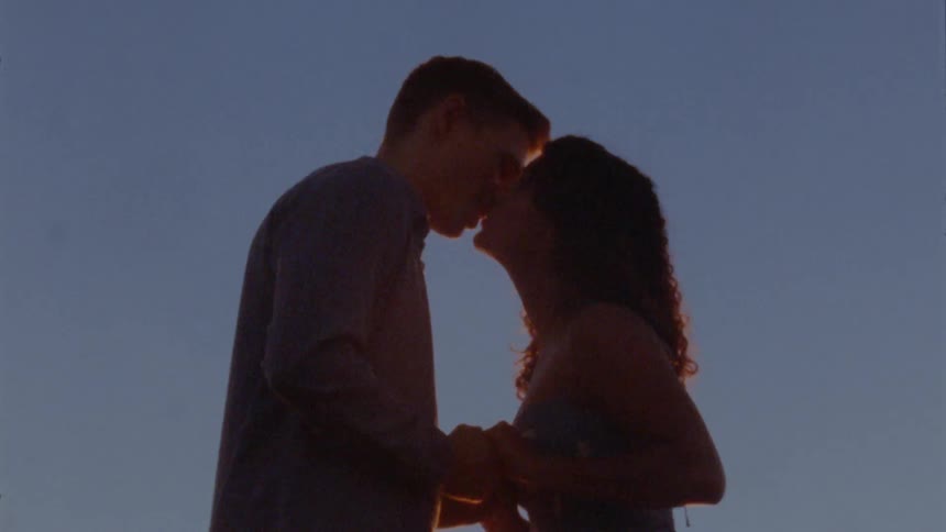A couple hold hands and lean in for a kiss