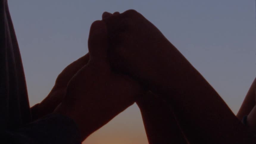 Two people holding hands in front of a sunset