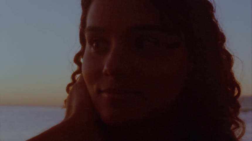 Man caresses womans cheek as they smile at each other while being back lit against red tinted sky