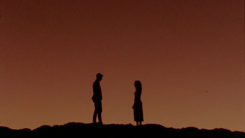 The silhouettes of a man and woman going towards one another and kissing and hugging as the sun sets behind them