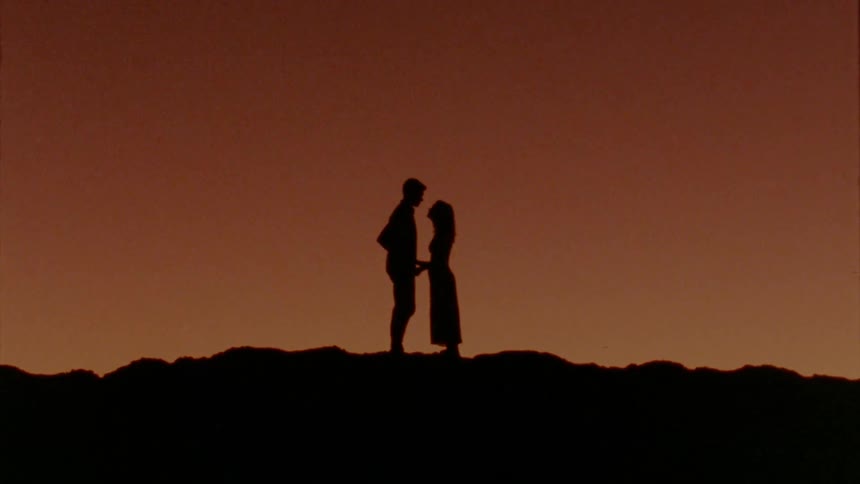 The silhouette of a man and woman on a ridge holding hands facing each other