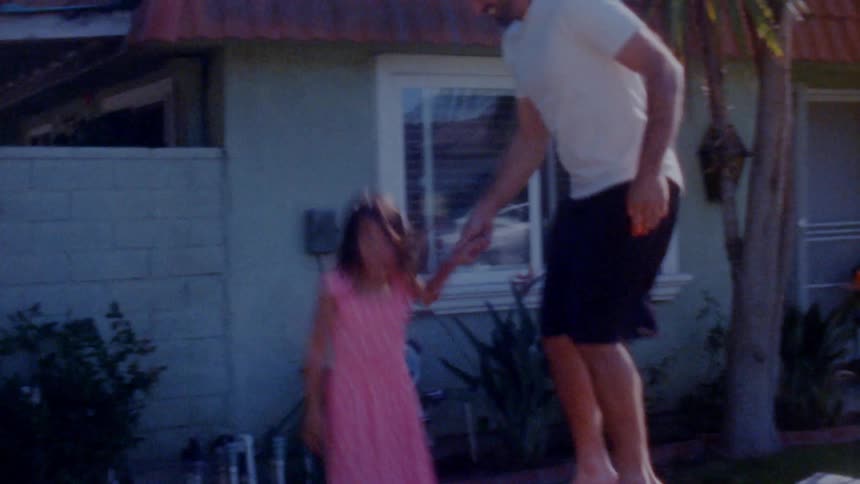 Speed up footage of father and daughter jumping over a trampoline at home caught on vintage film