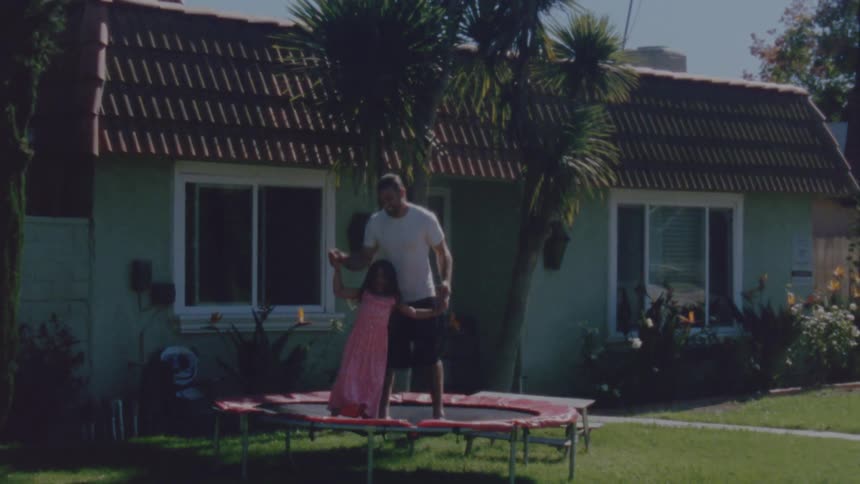 Father and daughter are jumping on a trampoline near their house