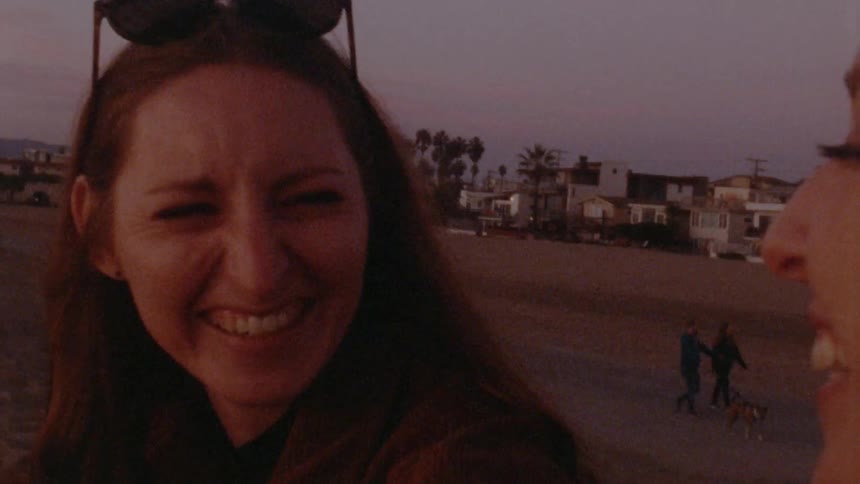 A woman with sunglasses on her head laughs and giggles with a friend as people walk by on the sand