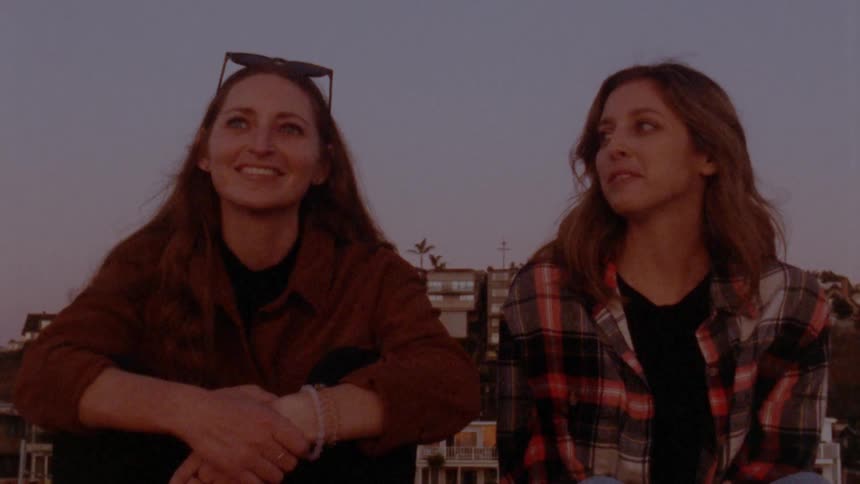 Two women laugh as they sit and chat in a neighborhood park