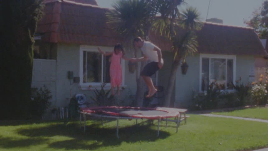Father and daughter juming on a trampoline on the front yard at home