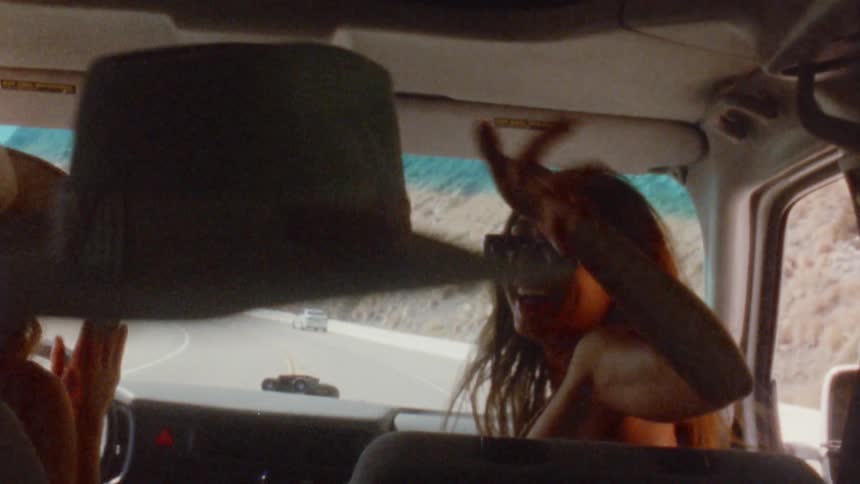 Girl throws a hat on the backseat of a car driving on a road to the beach