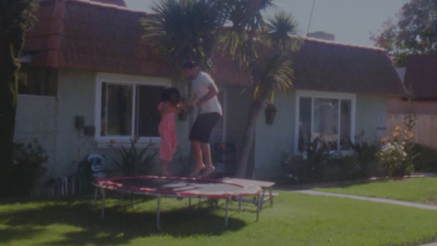Father and daughter are jumping on a trampoline in front of their house