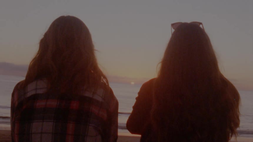 Two women stand on the shore and look out at the water