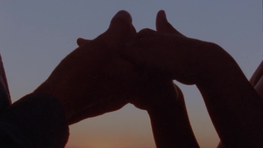 Two people touching hands outside at sunset