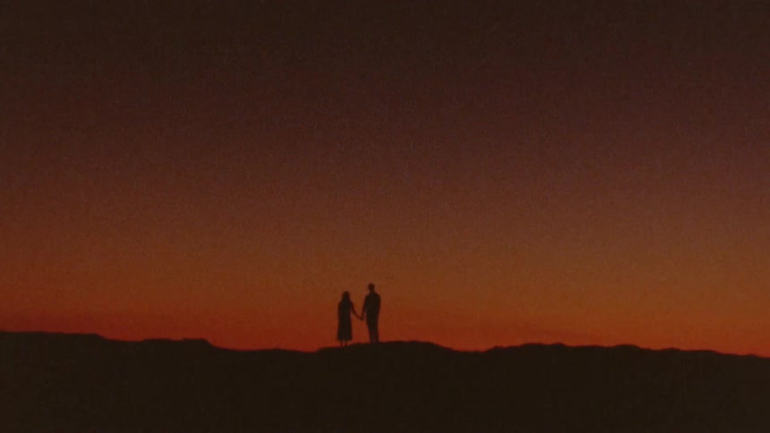A man and woman stand outside and hold hands and then the man turns towards her