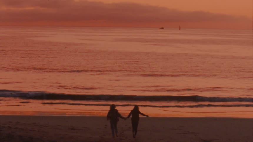 Two women run towards the ocean together