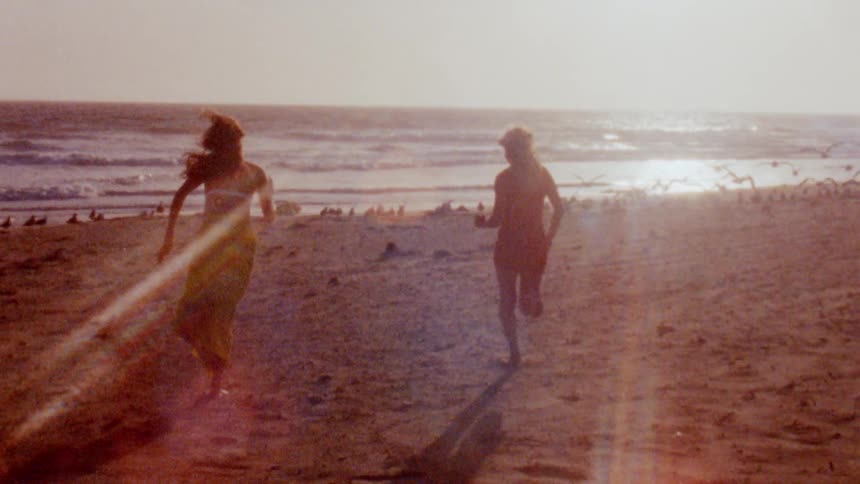 Two women running on a sandy beach with an american flag on a sunny summer day