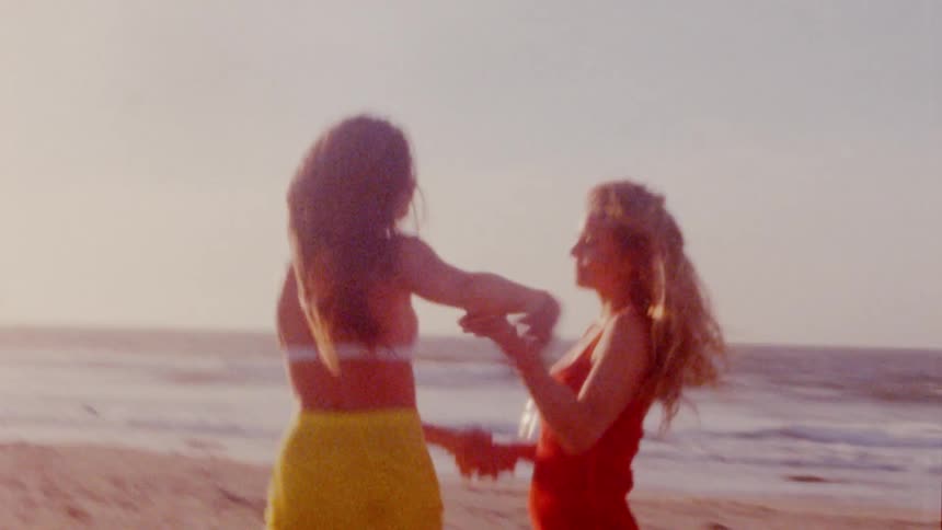 Two young friends holding hands and hugging on the beach next to the ocean