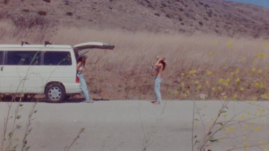 Two women chat while standing outside their van near a large hill