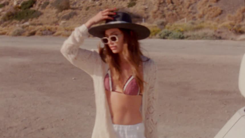 A woman holds onto her hat as she steps out of a car along a highway