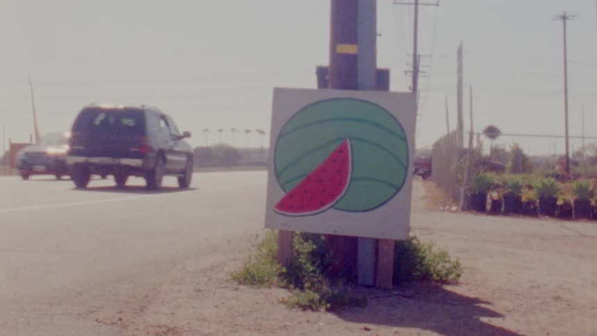 Cars drive past a sign with a watermelon drawn on it