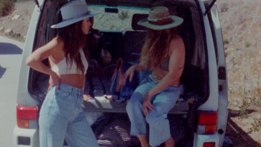 Two women hang out in the back of their van while parked along a highway