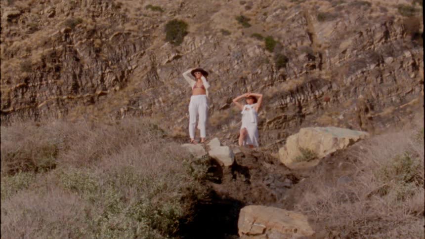 Two young women wearing white clotes standing on a cliff near the ocean