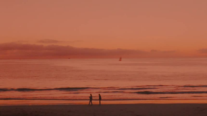 Women holding hands run on the beach and being silhouetted against the red sky next to ocean