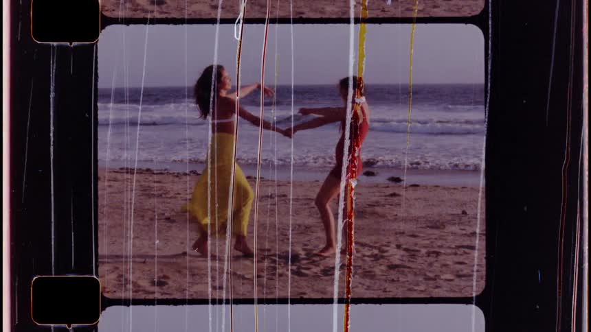 Two girls are holding hands and dancing on a beach as the waves roll in