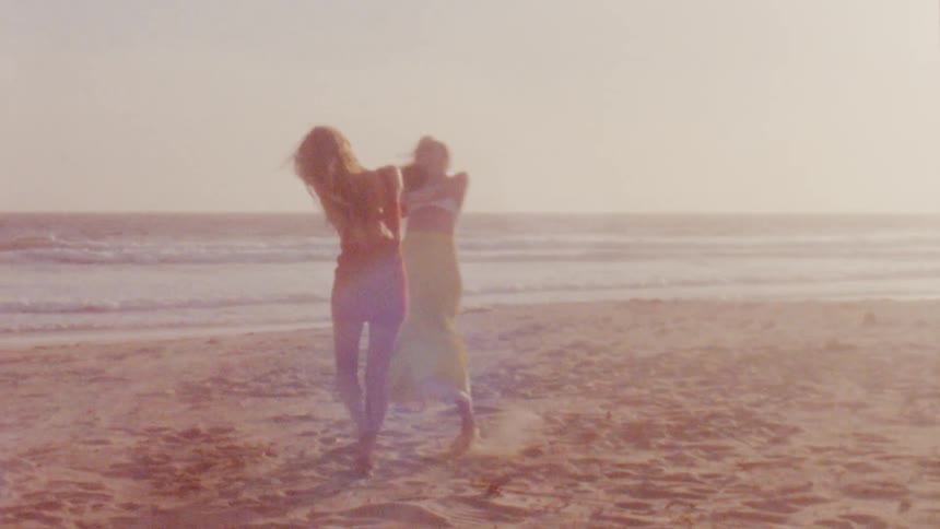 Two friends spin holding hands over the sand on a beach close to the ocean