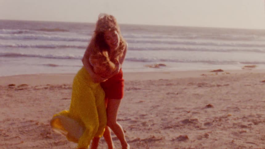 Two women play around smiling on beach on sunny day