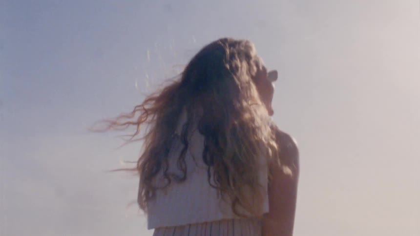 Two women walk on the beach raising their arms pointing in the bright sunshine