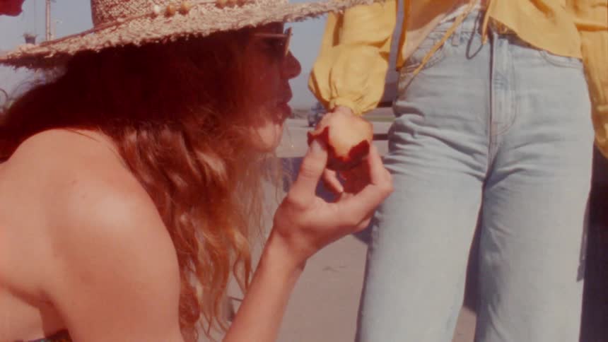 A woman is outside eating a fruit and talking to friends on a sunny day