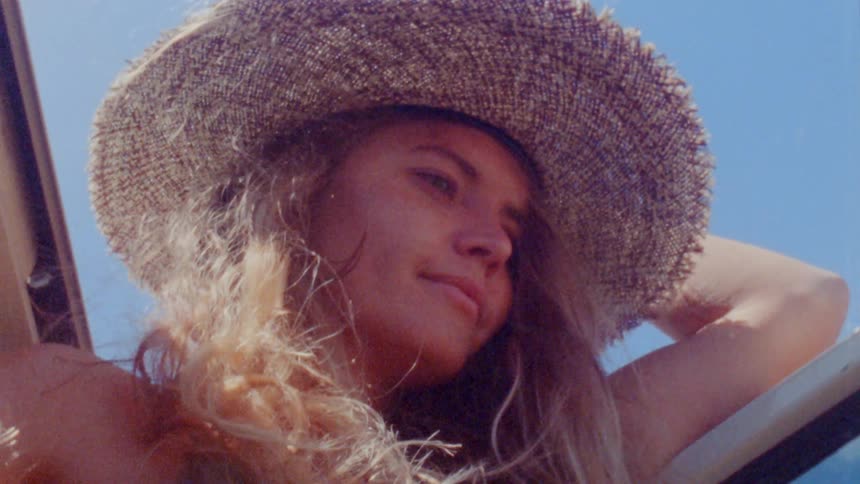 Blonde woman wearing sunhat sticks her head out of top of vehicle