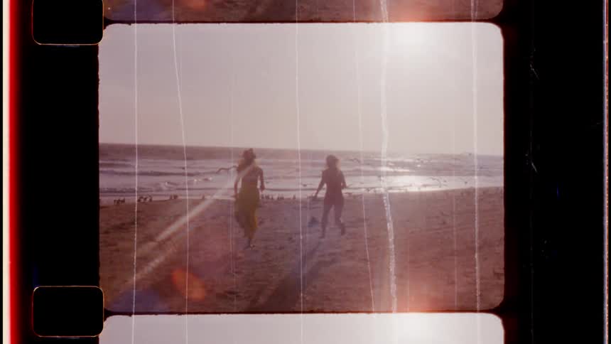 Two women with yellow and red dresses carrying towel run to beach while flock of seagulls flies away