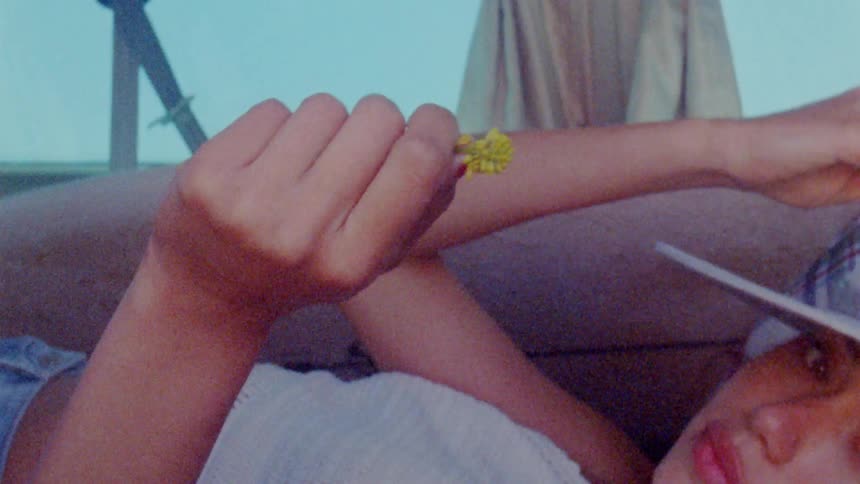 Woman lying on couch near windows talks and reaches out with yellow flower