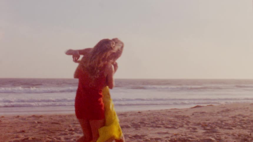 A woman chases her friend and they fall over in the sand